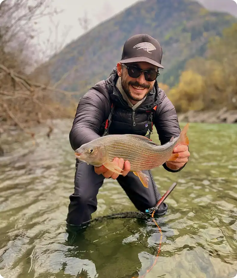 Giulio Pattaro kneeling in an alpine river holding a wild grayling