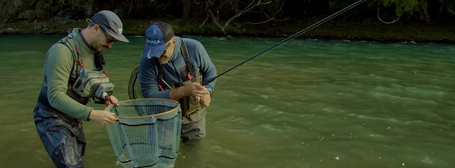 Two anglers netting a trout on an alpine river in the Dolomites