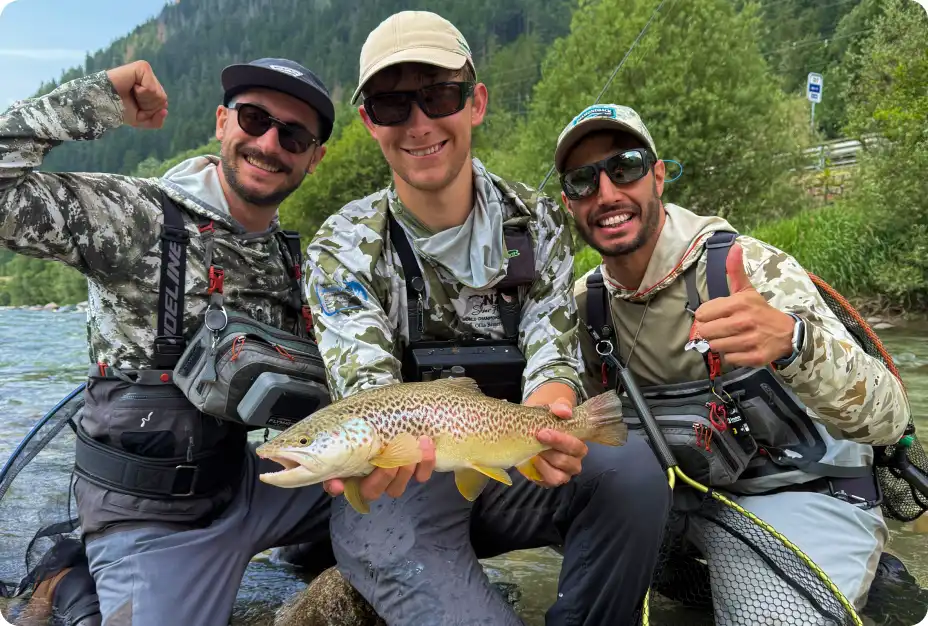 Three anglers wading in a river showing a wild brown trout caught during a full day guided trip