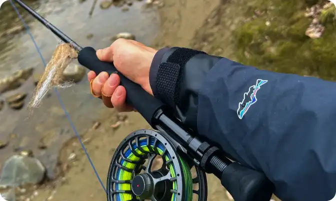 Angler holding a fly rod and reel pointed toward a mountain river